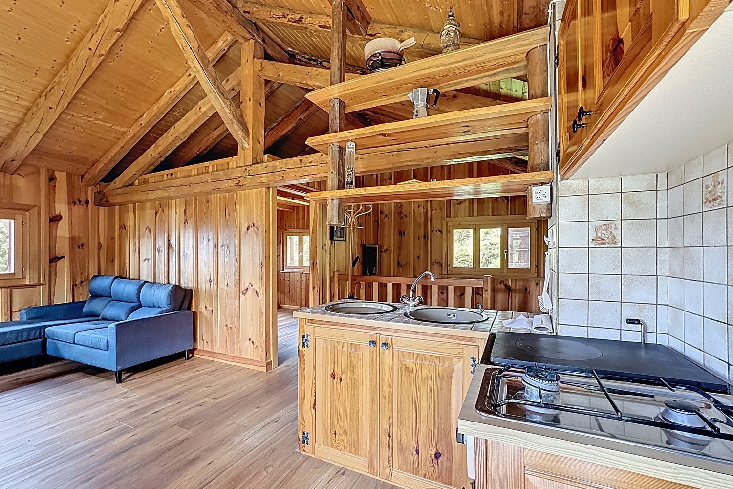 Cuisine au gaz du chalet : plan de travail carrelé, plaque à gaz, deux éviers inox, salon en arrière-plan.