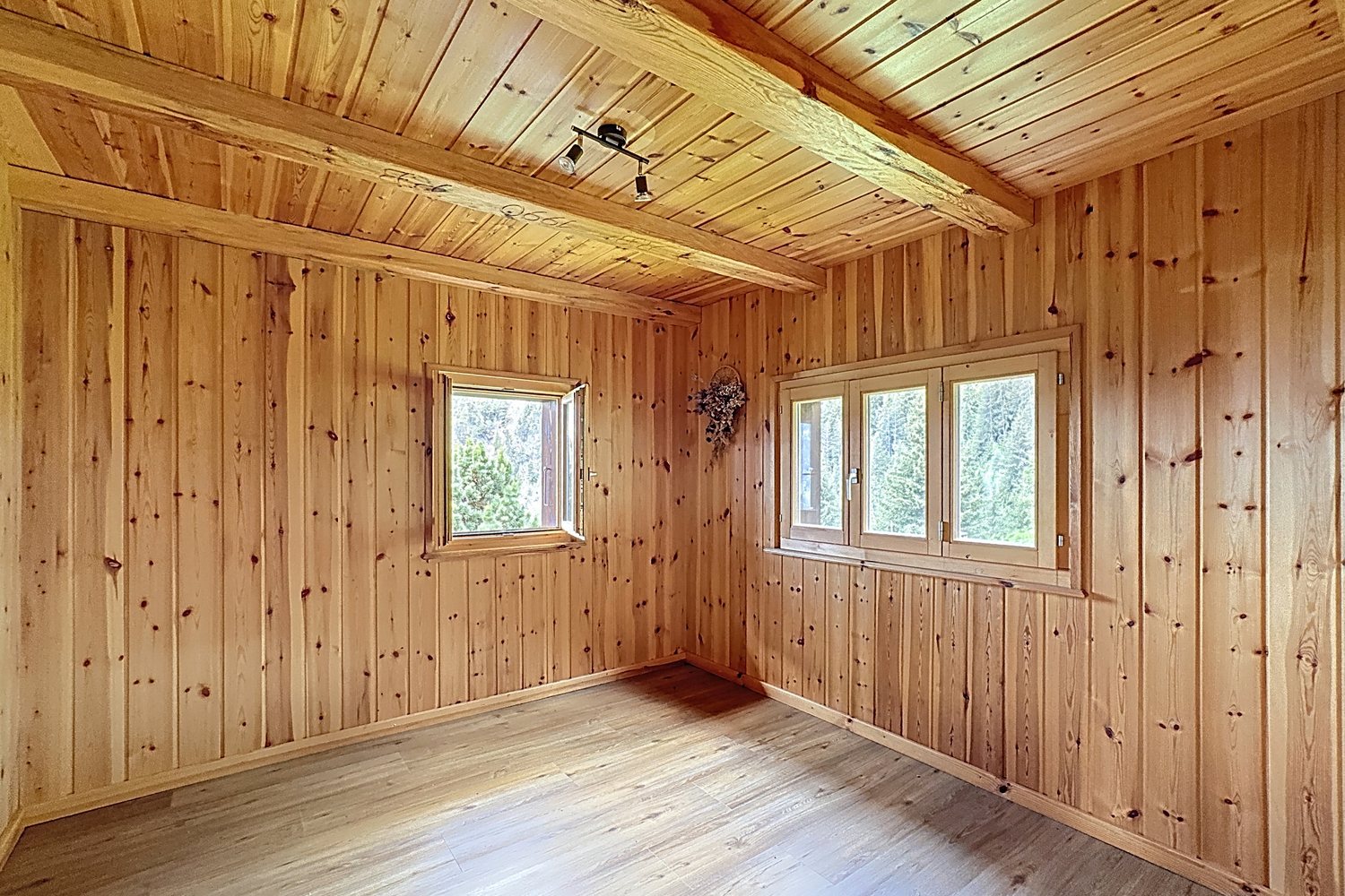 Seconde pièce lambrissée du chalet, vide, deux fenêtres sur les sapins, parquet clair.