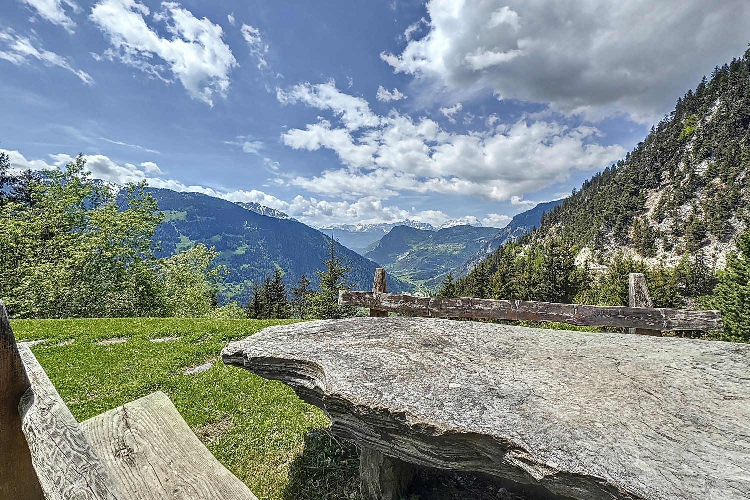 Table de pierre et banc de bois sur le pré, face à la vallée de Bagnes et aux sommets.